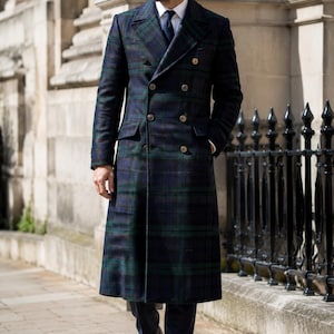 May include: A navy and green plaid double-breasted overcoat. The coat has gold-colored buttons and a classic lapel. The person is wearing a white shirt and a navy tie. Black leather shoes complete the outfit. The coat is long.