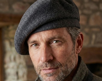 May include: A dark gray beret made of a soft, textured material. The hat is worn at an angle, with the brim resting on the forehead. The beret is a classic style, suitable for various occasions.