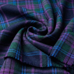 May include: Close-up of a folded fabric with a plaid pattern. The fabric features a combination of dark blue, green, purple, and blue lines. The edges of the fabric are frayed. The overall theme is textile.