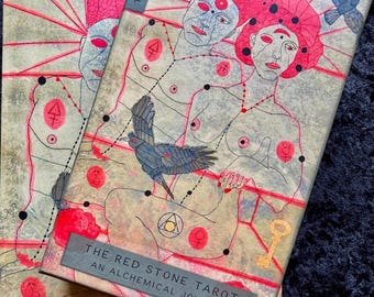 Puede incluir: Dos cajas de tarot apiladas con el texto "THE RED STONE TAROT - AN ALCHEMICAL JOURNEY". Las cajas presentan ilustraciones de figuras con acentos rojos, pájaros y diseños geométricos. El nombre del artista, "LINDA HILL", es visible.