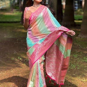 May include: A multi-colored saree featuring horizontal stripes in pastel pink, mint green, and peach. The fabric is adorned with intricate silver metallic woven patterns and a wide, vibrant hot pink border with detailed floral motifs and tassels.