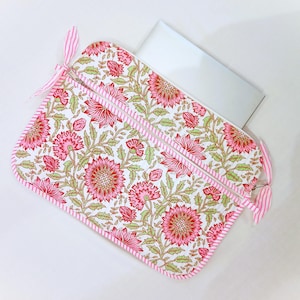 May include: A floral laptop sleeve with a white background. The sleeve features a pink and green floral pattern with a pink striped border and zipper. Pink striped ribbons are attached to the zipper pulls.