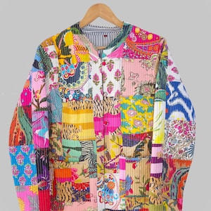 May include: A patchwork jacket with a vibrant mix of floral, paisley, and animal print patterns in pink, yellow, blue, and green. The jacket has a striped lining and two front pockets. It is hanging on a wooden hanger.