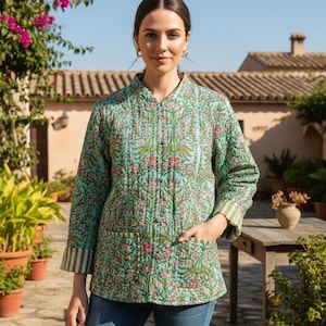 May include: A quilted jacket in a floral pattern with shades of teal, pink, and green. The jacket has a mandarin collar, long sleeves with striped cuffs, and two front pockets. The jacket is worn with blue jeans.