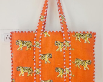 Könnte beinhalten: Orangefarbene Tragetasche mit einem sich wiederholenden Muster aus gelben und schwarzen Tigern. Die Tasche hat passende orangefarbene Griffe und eine weiß-rot gestreifte Bordüre. Die Tasche hängt an einer weißen Wand.