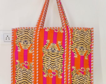 Könnte beinhalten: Eine lebendige Tragetasche mit einem sich wiederholenden Tigermuster auf einem gestreiften Hintergrund in Orange und Pink. Die Tasche hat passende orangefarbene Griffe mit weiß-rosa gestreiften Zierleisten. Die Tasche ist aus einem gesteppten Stoff gefertigt.