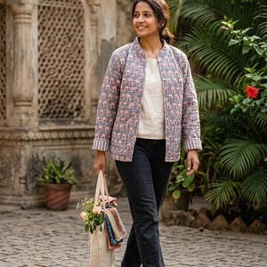 Peut inclure: Veste matelassée grise à motif floral rose. La veste est portée sur un haut blanc, associée à un jean foncé et des bottines marron. Un sac fourre-tout en toile avec des fleurs et du tissu est porté.