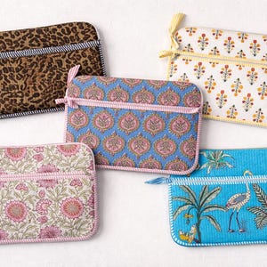 May include: Five rectangular fabric pouches with zipper closures. Designs include a leopard print, floral patterns, and a blue pouch with a tropical scene. Each pouch has a contrasting trim and a small fabric loop.