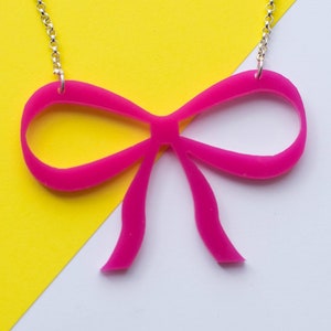 May include: A silver chain necklace with a large, bright pink bow pendant. The bow is made of acrylic and has a glossy finish.