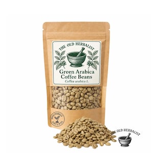 May include: A brown paper pouch containing raw green Arabica coffee beans. The label features the text THE OLD HERBALIST, an illustration of a mortar and pestle, and the words Green Arabica Coffee Beans and Coffea arabica L. A pile of beans sits in front.