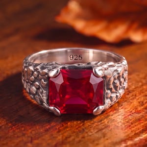 May include: A silver ring featuring a large, rectangular, faceted red gemstone set in a textured, organic-looking band. The interior of the band is clearly stamped with the number 925, indicating sterling silver composition for this jewellery piece.