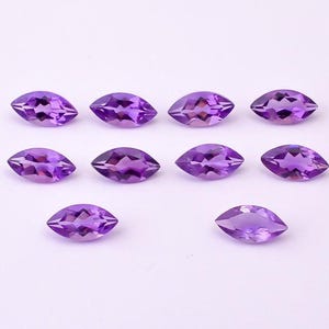 May include: Ten marquise-cut amethyst gemstones, each displaying a deep purple hue. The gemstones are arranged on a white surface, showcasing their faceted surfaces and symmetrical shapes. Ideal for jewelry making.