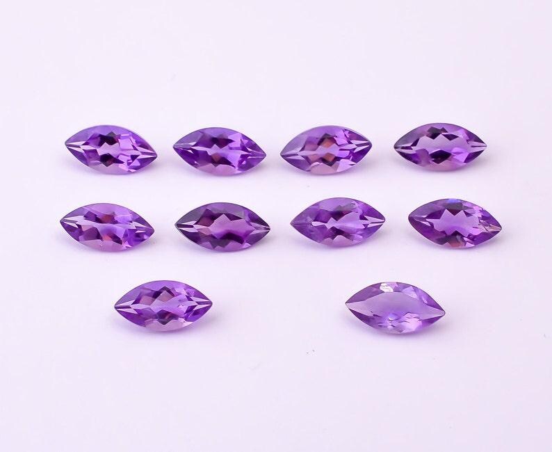 May include: Ten marquise-cut amethyst gemstones, each displaying a deep purple hue. The gemstones are arranged on a white surface, showcasing their faceted surfaces and symmetrical shapes. Ideal for jewelry making.
