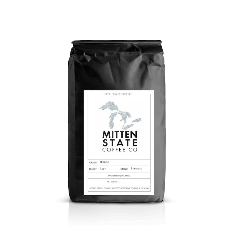 May include: A black coffee bag with a white label featuring the text "MITTEN STATE COFFEE CO." and a map outline. The label also indicates "Blonde" origin, "Light" roast, and "Standard" grind. The bag is filled with fresh roasted coffee.