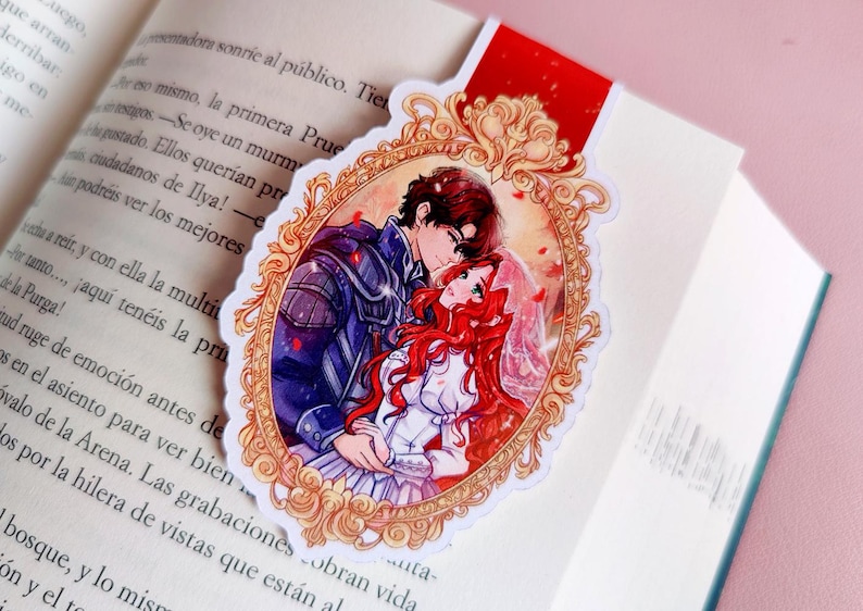 May include: A bookmark featuring a romantic anime-style illustration of a couple embracing within an ornate gold frame. The bookmark is red at the top and is placed in an open book.