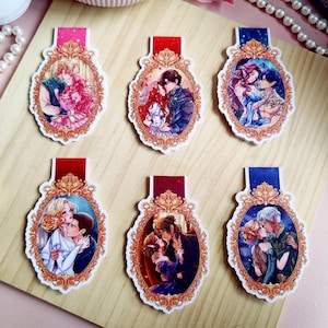 May include: Six decorative bookmarks with romantic illustrations. Each bookmark features a different couple in an ornate, oval frame with a red or blue top. The illustrations depict couples embracing, with vibrant colors and detailed artwork.