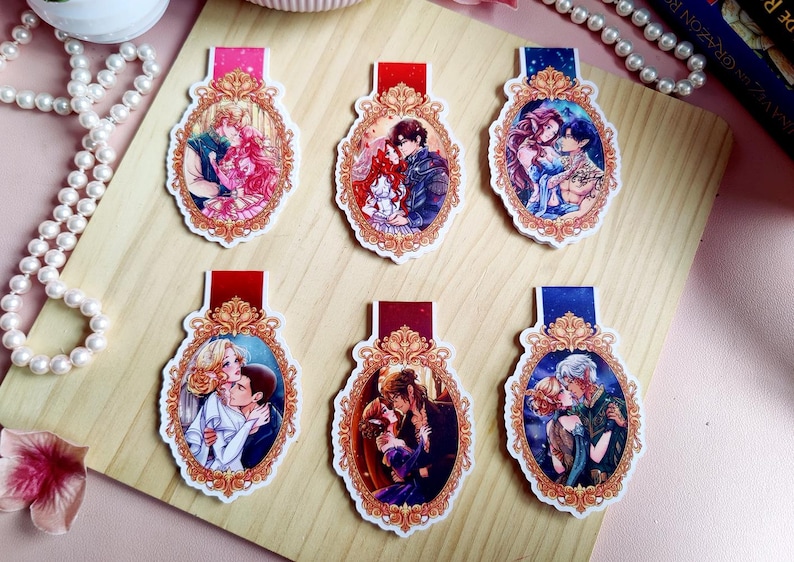 May include: Six decorative bookmarks with romantic illustrations. Each bookmark features a different couple in an ornate, oval frame with a red or blue top. The illustrations depict couples embracing, with vibrant colors and detailed artwork.
