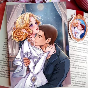 Op de afbeelding: Een bladwijzer met een anime-stijl illustratie van een stel dat elkaar omhelst. De vrouw heeft blond haar en draagt een witte jurk. De man draagt een zwarte jas. Een kleinere, ingelijste afbeelding van het stel is ook zichtbaar.