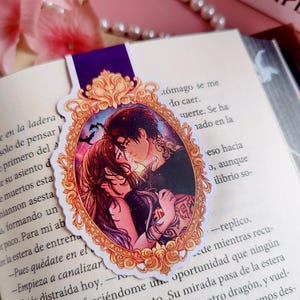 Puede incluir: Marcap&aacute;ginas decorativo con una ilustraci&oacute;n de una pareja abraz&aacute;ndose dentro de un marco dorado ornamentado. El marcap&aacute;ginas tiene una parte superior morada y est&aacute; colocado en un libro abierto. Tema rom&aacute;ntico.