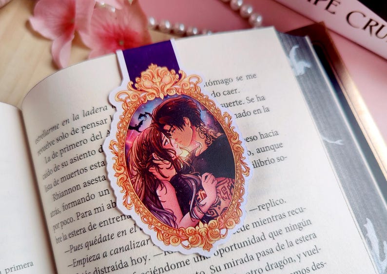 Puede incluir: Marcap&aacute;ginas decorativo con una ilustraci&oacute;n de una pareja abraz&aacute;ndose dentro de un marco dorado ornamentado. El marcap&aacute;ginas tiene una parte superior morada y est&aacute; colocado en un libro abierto. Tema rom&aacute;ntico.