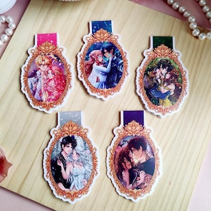 Puede incluir: Cinco marcap&aacute;ginas decorativos con ilustraciones rom&aacute;nticas de estilo anime. Cada marcap&aacute;ginas presenta una pareja diferente en un marco ovalado decorativo con un borde dorado. Los marcap&aacute;ginas tienen pesta&ntilde;as de diferentes colores.