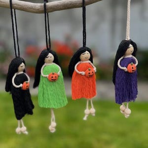 Può includere: Quattro ornamenti di Halloween fatti a mano. Ogni bambola ha capelli di filo nero, una testa di legno e un vestito colorato. Le bambole tengono piccole decorazioni di zucca arancione. Le bambole sono appese a un ramo di legno.