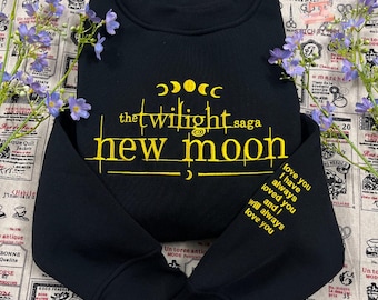 May include: Black sweatshirt with yellow embroidered text reading "the twilight saga new moon." The design includes crescent moons and stars. The sleeve has the text "love you I have always loved you and I will always love you."