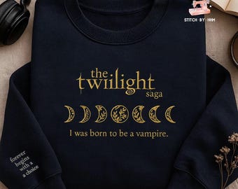 May include: Navy blue sweatshirt with gold text reading "the twilight saga" and "I was born to be a vampire." The design includes moon phases. The left sleeve has the text "forever begins with a choice."