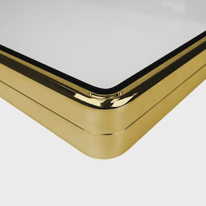 May include: Close-up of a gold-colored, rectangular object with a white surface. The object has rounded corners and a shiny, metallic finish. The corner is in sharp focus, highlighting the craftsmanship.