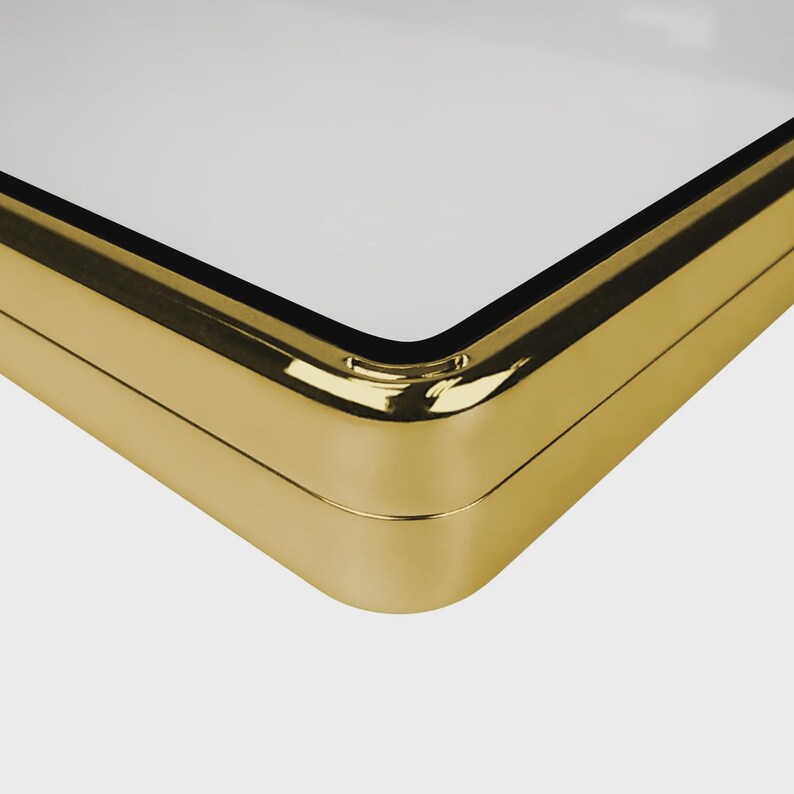 May include: Close-up of a gold-colored, rectangular object with a white surface. The object has rounded corners and a shiny, metallic finish. The corner is in sharp focus, highlighting the craftsmanship.