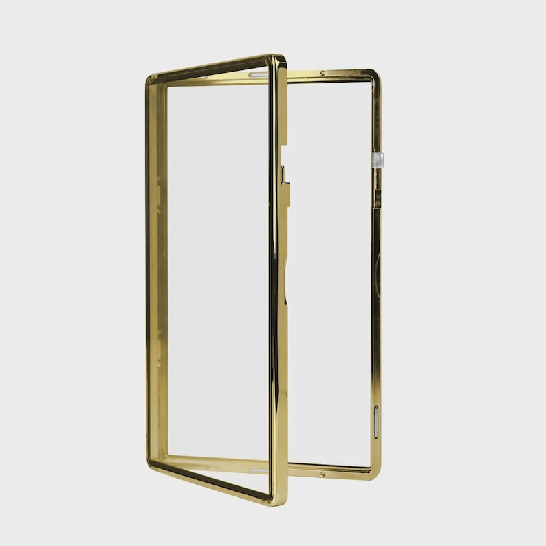 May include: A gold-colored rectangular frame with a clear, transparent center. The frame is open, with one side slightly ajar, revealing the interior. The design is sleek and modern, with a polished finish.