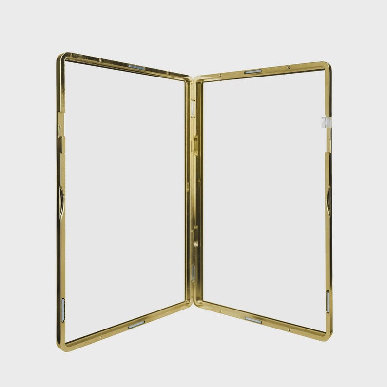 May include: A gold-colored, hinged picture frame, open to reveal two clear panels. The frame has a rectangular shape with rounded corners and a shiny finish. The frame is designed to display two photos or images.