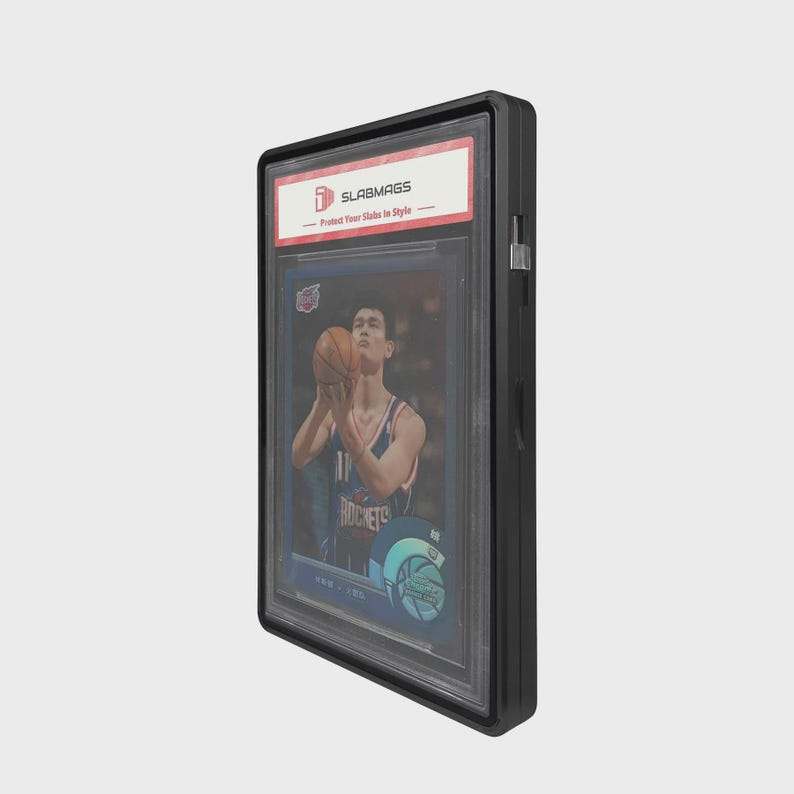 Puede incluir: Una funda protectora negra con una tarjeta de baloncesto graduada en su interior. La tarjeta presenta a un jugador con la camiseta de los Rockets sosteniendo un bal&oacute;n. La funda tiene una etiqueta blanca con el texto "SLABMAGS - Protect Your Slabs in Style".
