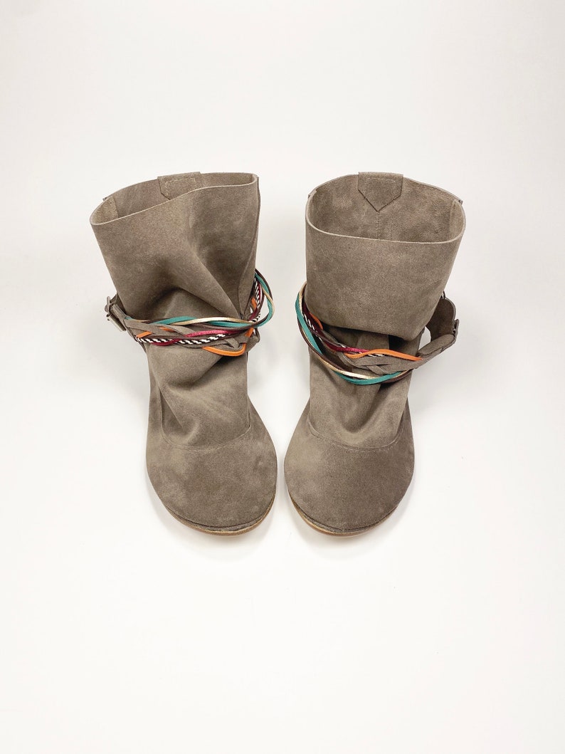 May include: A pair of gray suede ankle boots with colorful braided straps around the ankle.
