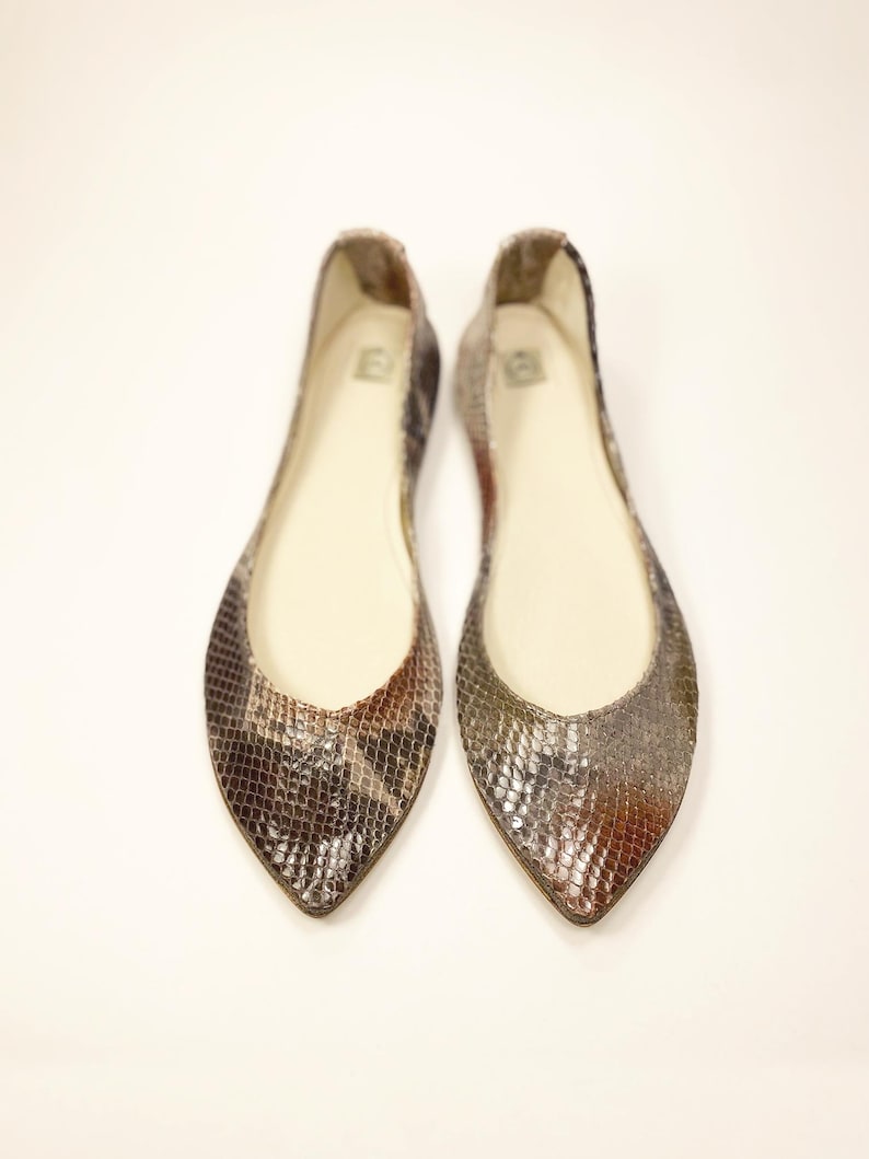 Peut inclure: Une paire de ballerines &agrave; bout pointu avec un motif peau de serpent dans les tons marron, gris et or. Les chaussures ont un petit talon et un int&eacute;rieur de couleur neutre. Les ballerines sont pr&eacute;sent&eacute;es sur fond blanc.