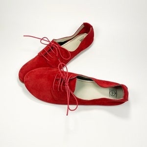 May include: A pair of red suede lace-up shoes with white laces. The shoes have a simple design and are made of soft, comfortable material.