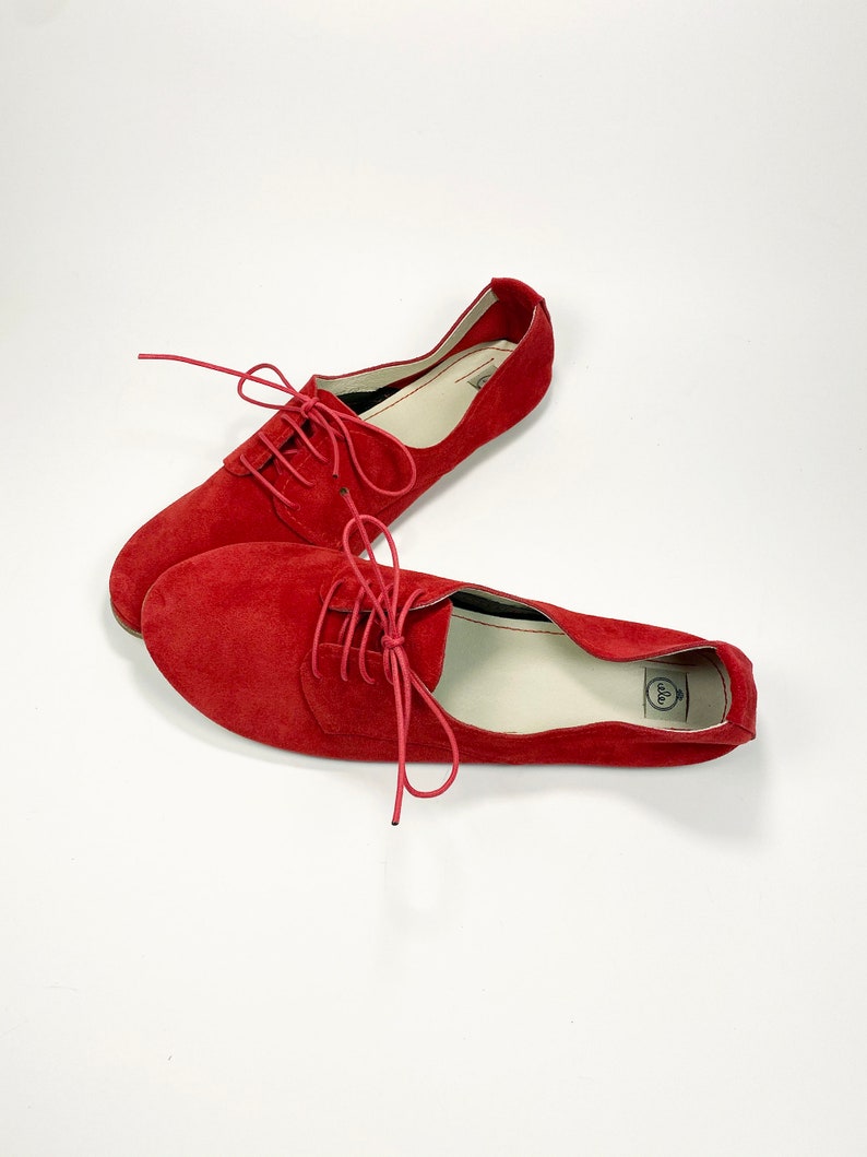 May include: A pair of red suede lace-up shoes with white laces. The shoes have a simple design and are made of soft, comfortable material.