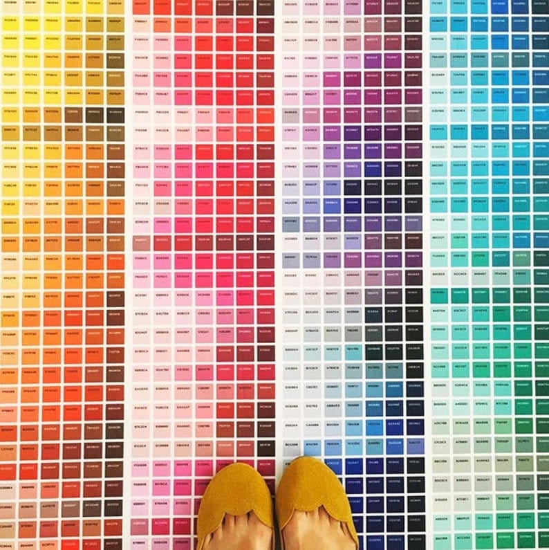 May include: A large color chart with hundreds of small squares of different colors, arranged in a rainbow pattern. Two yellow shoes are in the foreground, with the toes pointing towards the camera.