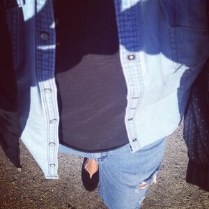 May include: A blue denim jacket with a black t-shirt and blue jeans underneath. The person is wearing black flats.