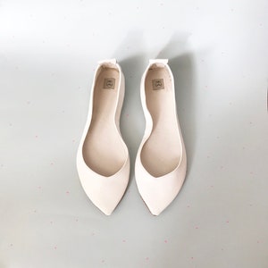 May include: A pair of white leather ballet flats with pointed toes. The flats have a simple design and are made of a soft, supple leather.