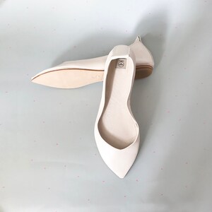 May include: A pair of white leather ballet flats with pointed toes. The flats are laid out on a light blue background with a white polka dot pattern.