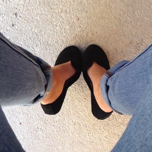May include: A pair of black ballet flats with a pointed toe. The flats are worn by a person wearing blue jeans.