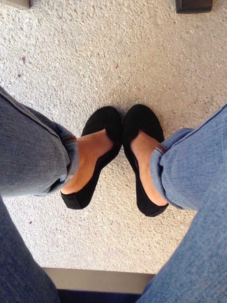 May include: A pair of black ballet flats with a pointed toe. The flats are worn by a person wearing blue jeans.
