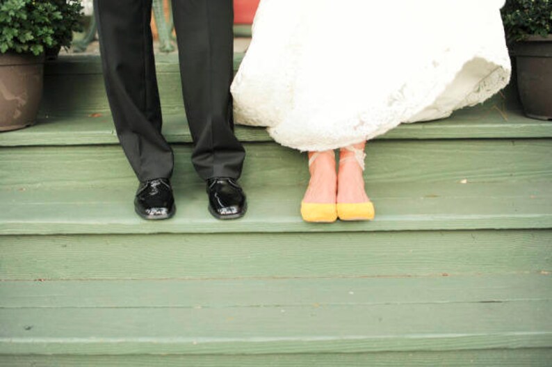May include: A bride and groom stand on a set of green wooden steps. The bride is wearing a white wedding dress and yellow shoes. The groom is wearing a black suit and black shoes.