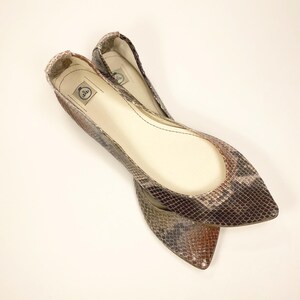 Peut inclure: Deux ballerines &agrave; bout pointu avec un motif peau de serpent dans les tons marron, gris et beige. Les chaussures ont un petit talon et un int&eacute;rieur lisse blanc cass&eacute;. Ces chaussures sont con&ccedil;ues pour le confort et le style.