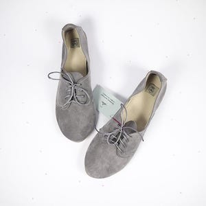 May include: A pair of gray suede lace-up shoes with a rounded toe.