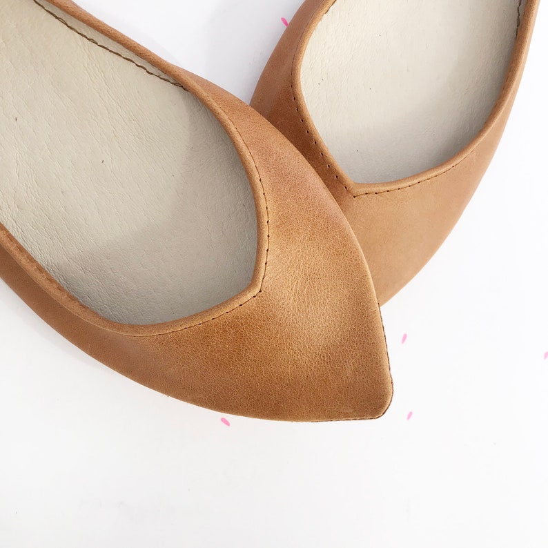May include: A pair of brown leather ballet flats with pointed toes. The flats have a light brown leather lining and a white insole.