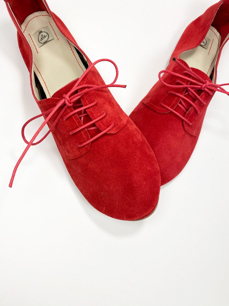 May include: A pair of red suede lace-up shoes with a low heel. The shoes have a simple design and are made of soft, comfortable material.