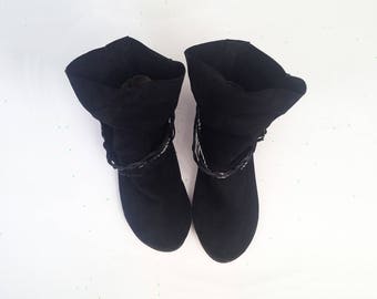 May include: A pair of black suede ankle boots with a folded-down top and a braided detail around the ankle.
