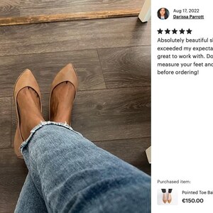 May include: A pair of tan pointed toe ballet flats worn by a person with blue jeans. The shoes are on a wooden floor. The text "Pointed Toe Ballet Flats in Tan Soft Ital... &euro;150.00" is visible.